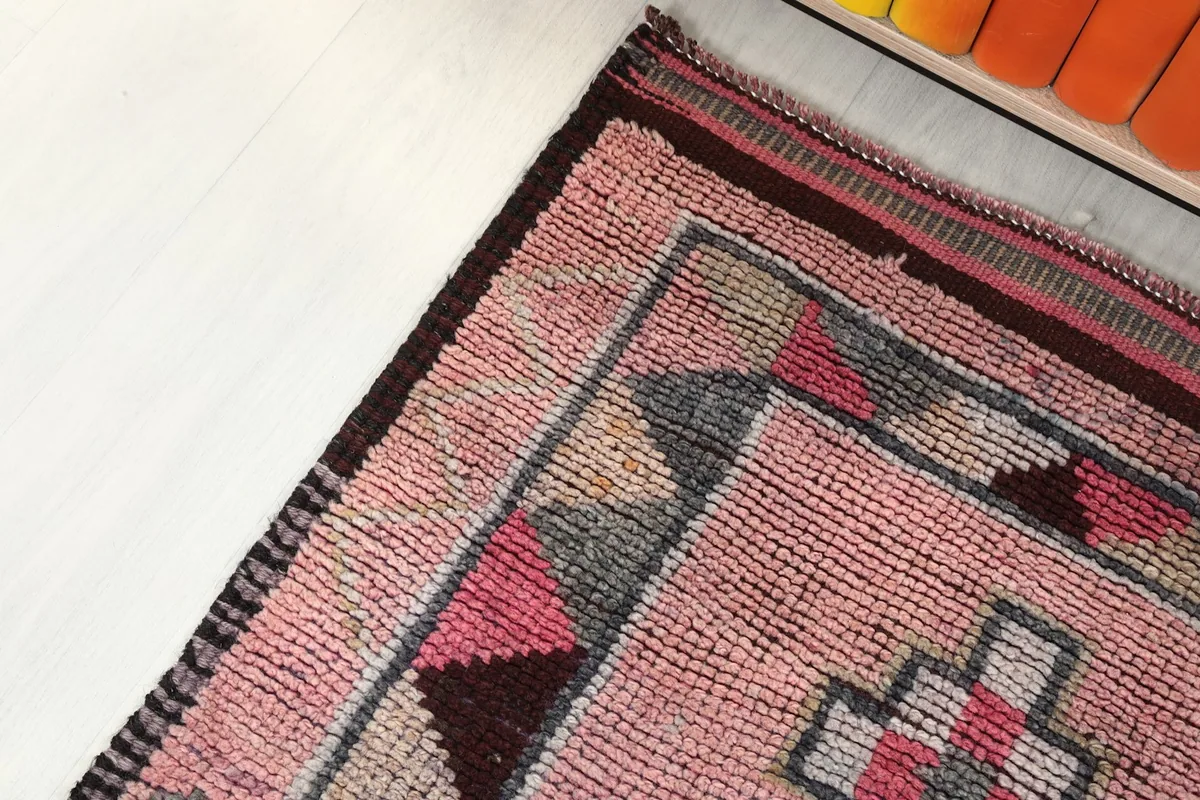 Corner detail of the runner rug, highlighting the worn edges and geometric border design