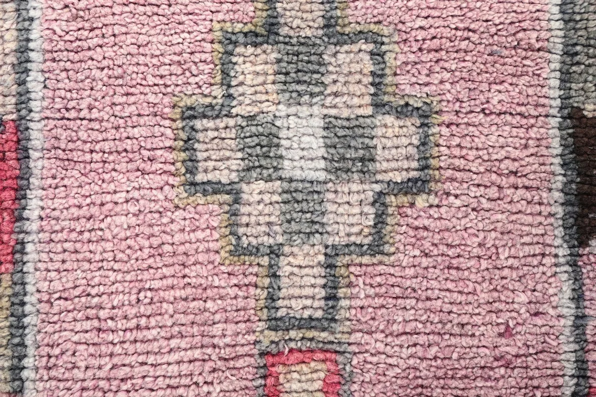 Close-up of the low wool pile and hand-knotted texture of a geometric motif in rose and gray