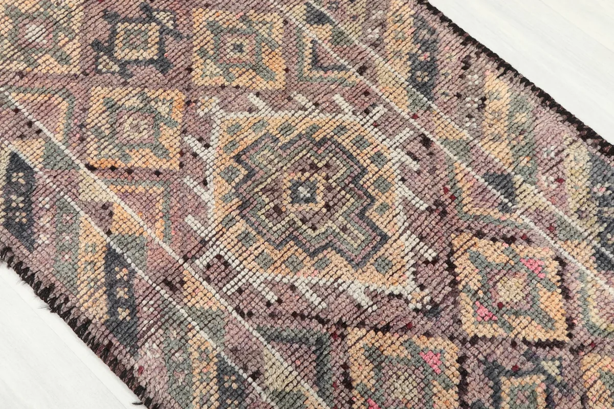 Diagonal view of the runner rug's central geometric motifs in purple, gray, beige, and subtle red.