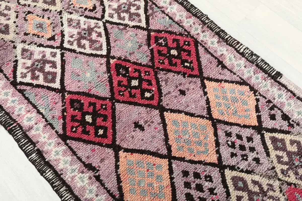 Angled close-up of the rug's central design, featuring various diamond and tribal motifs in red, orange, and black.