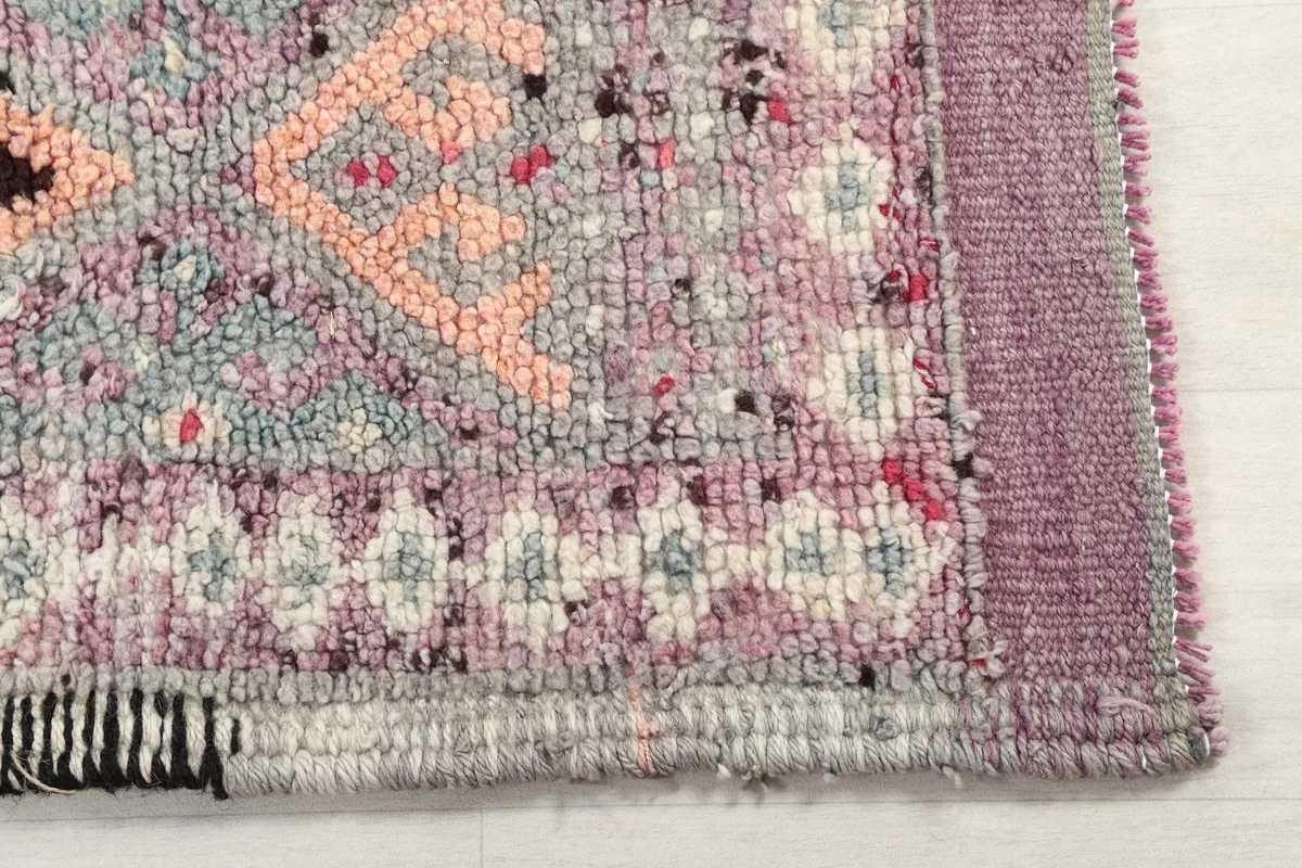 Detail of the rug's edge and border, showing the hand-knotted texture and the purple and gray tones.