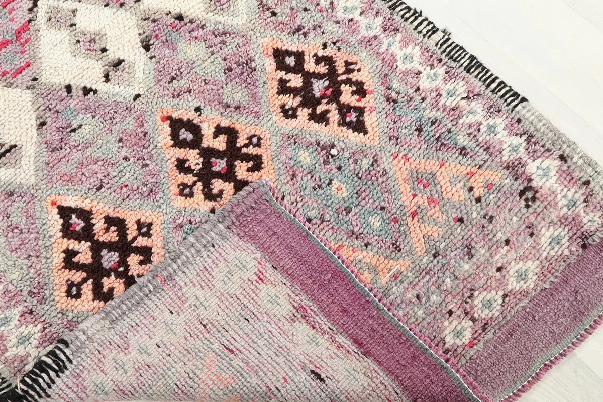 Corner of the rug folded back, revealing the hand-knotted construction on a cotton foundation from the reverse side.