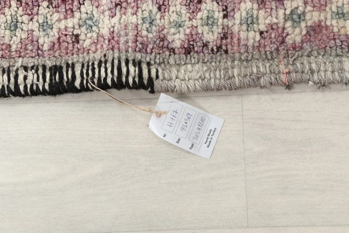 Detail of the rug's edge with a tag displaying its dimensions in centimeters and inches.