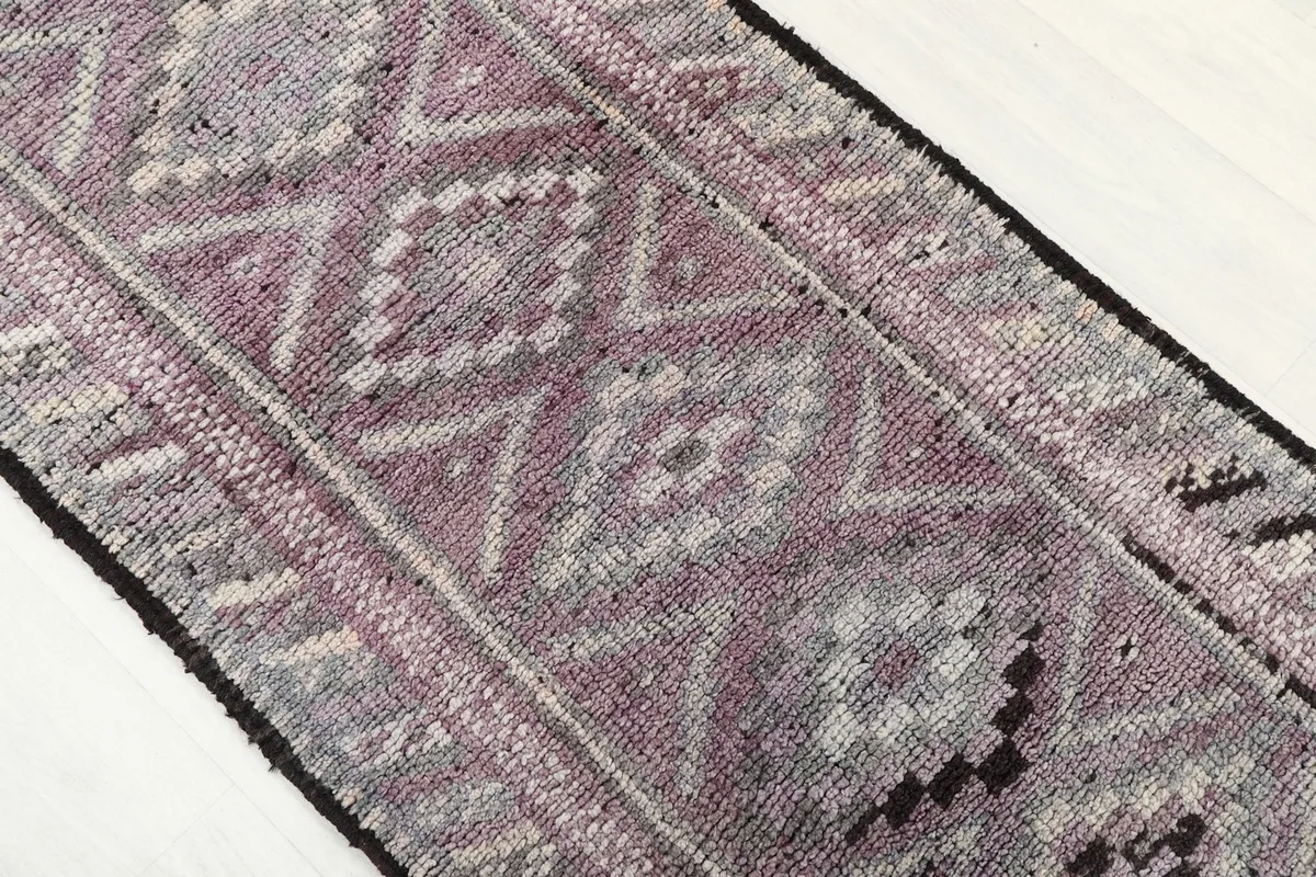 Close-up of the rug's geometric motifs in rose, gray, and cream, with black accents and visible texture.