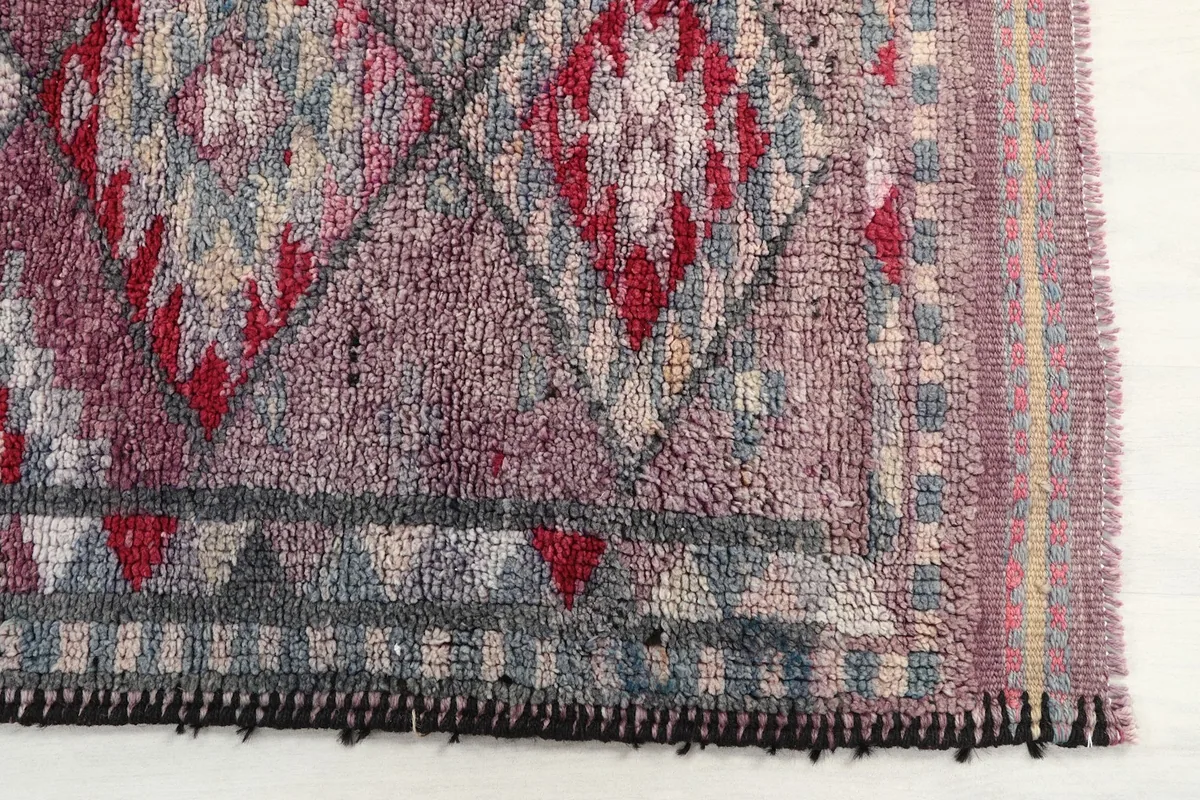 Detailed view of the rug's tribal geometric patterns in rose, red, gray, and beige, showing edge finishing.