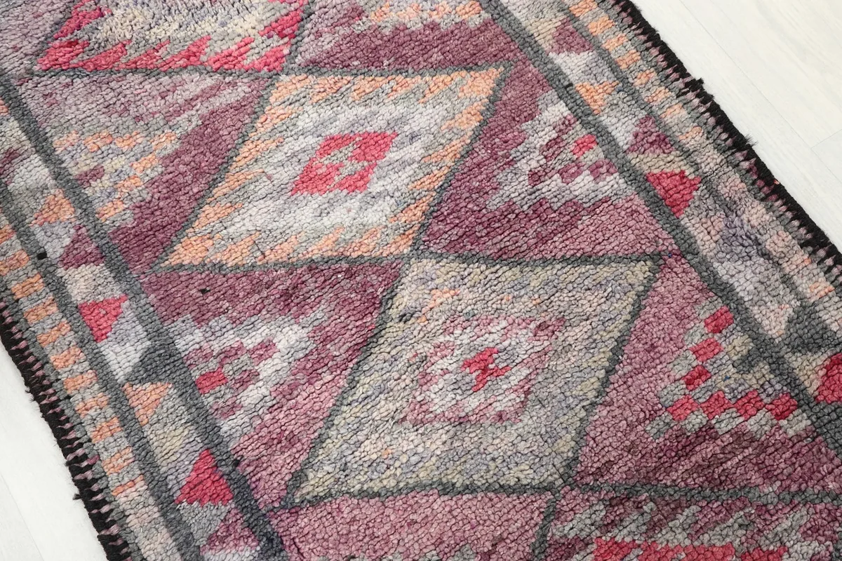 Close-up of the rug's surface, showing the blend of rose, gray, and orange tones within the diamond motifs.