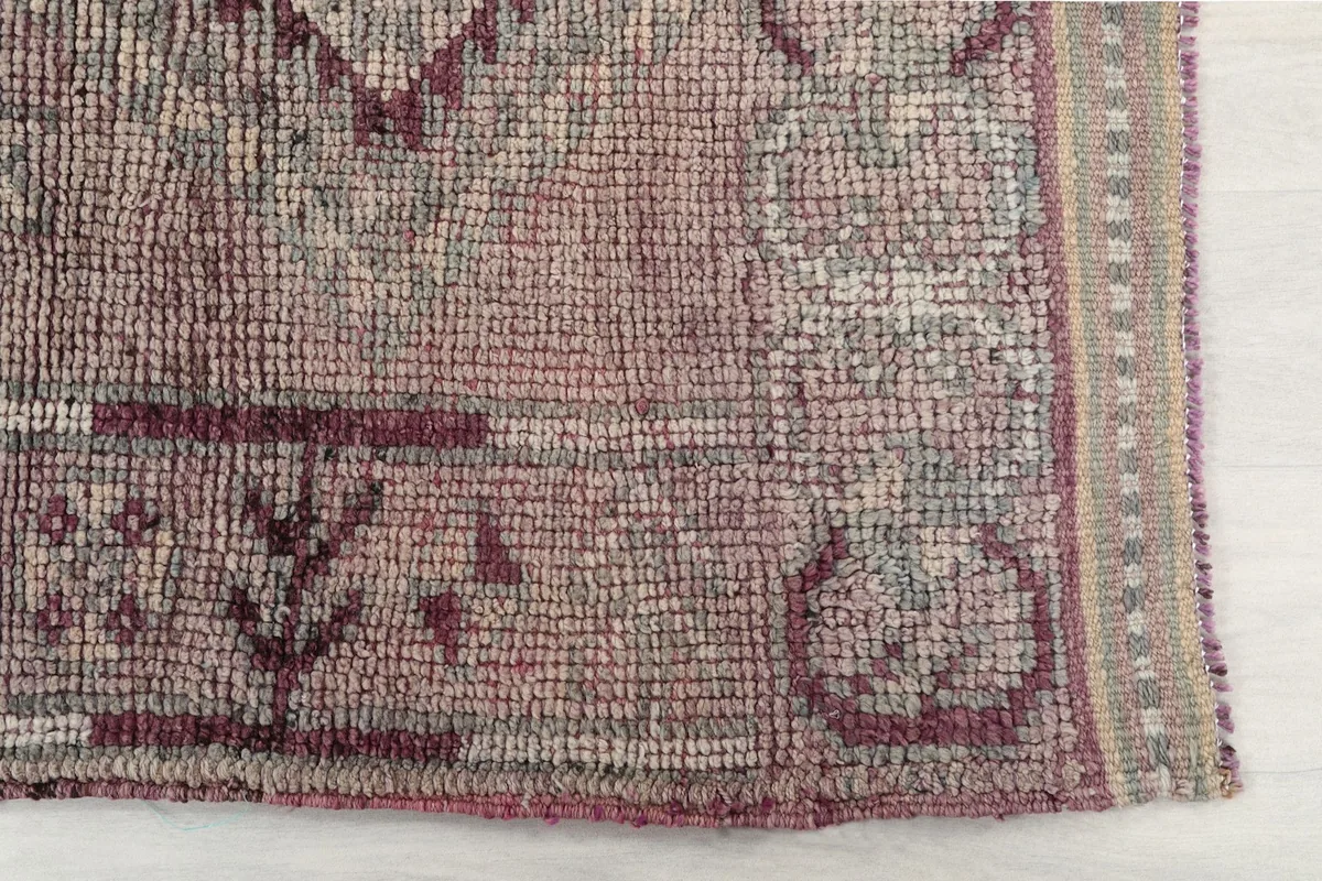 Detailed view of the rug's end, showing the low pile and border design in rose and tan