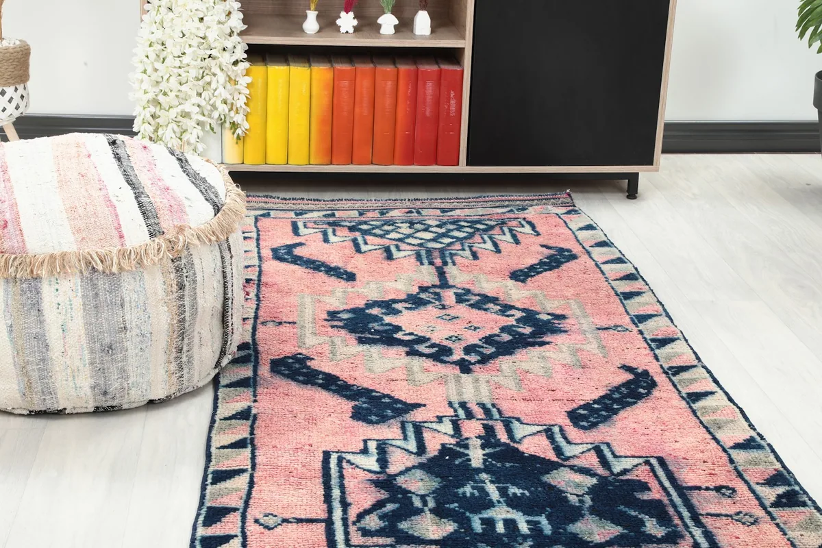 Close-up view of the runner rug's end in a room, next to a striped pouf and wooden shelving