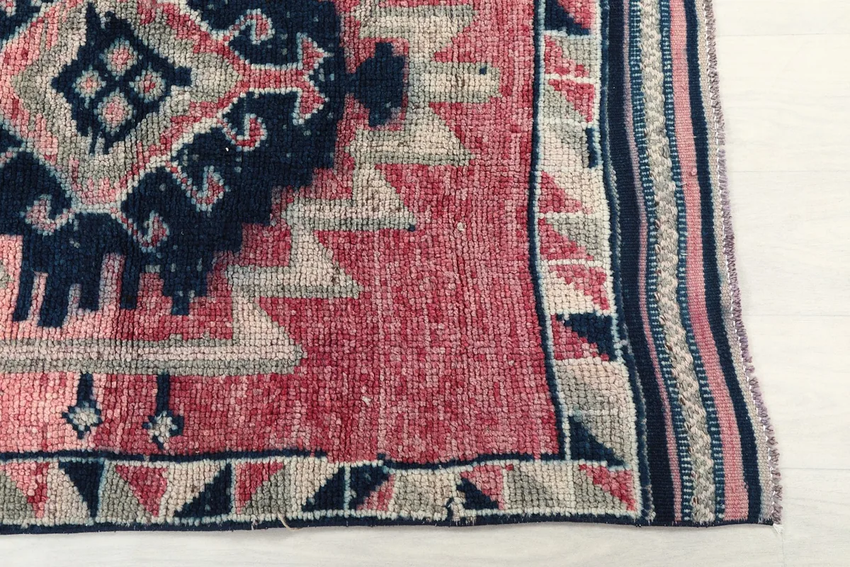 Detailed view of the rug's border and a section of the pink field with navy and gray geometric motifs