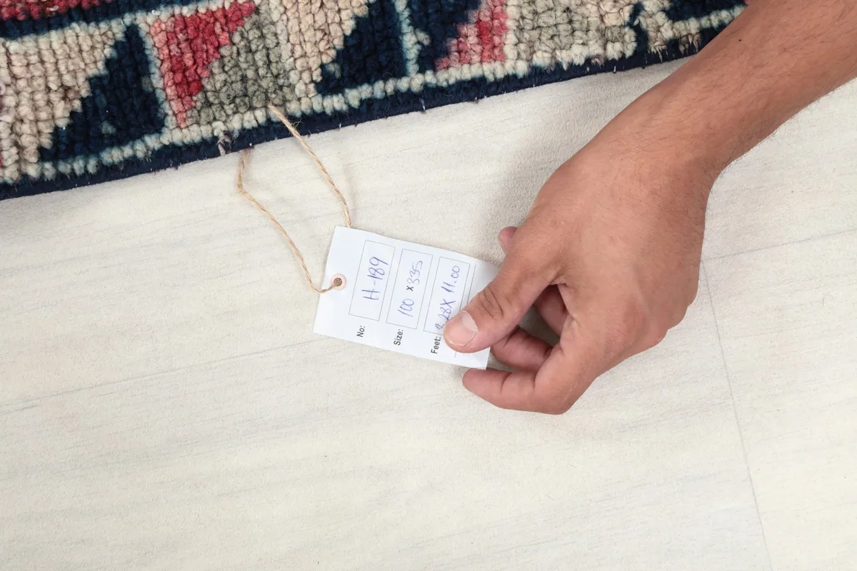 Hand holding a tag with the rug's size and details, indicating its origin and materials