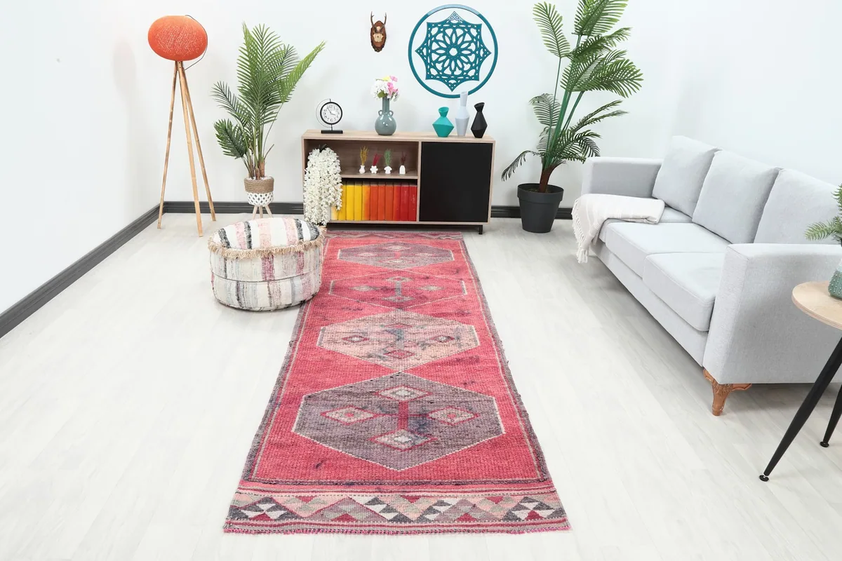 Vintage Anatolian runner rug in a hallway setting, showing its faded red and geometric patterns.