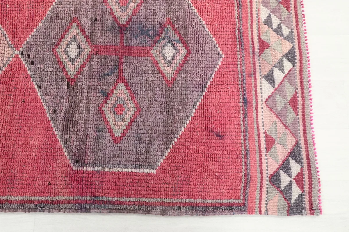 Detail of one geometric medallion in purple and gray, with a small section of the border pattern.