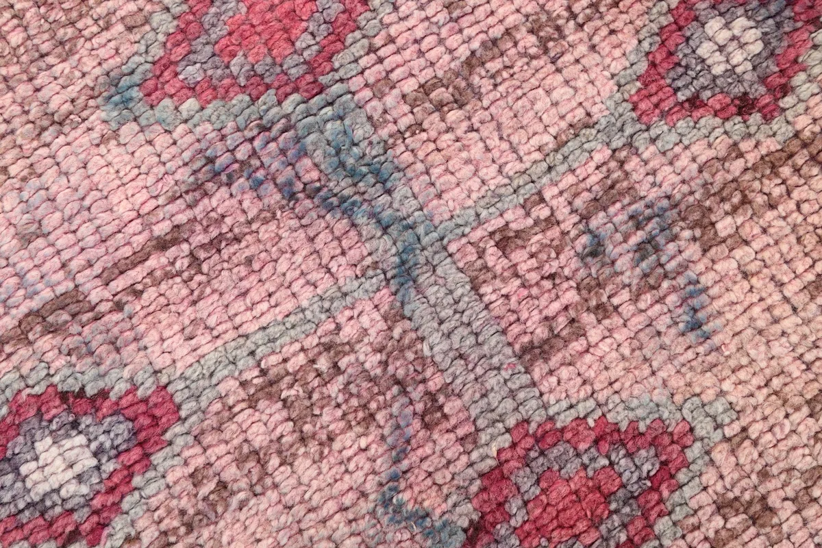 Macro view of the hand-knotted wool pile, revealing the texture and colors of the faded rug.