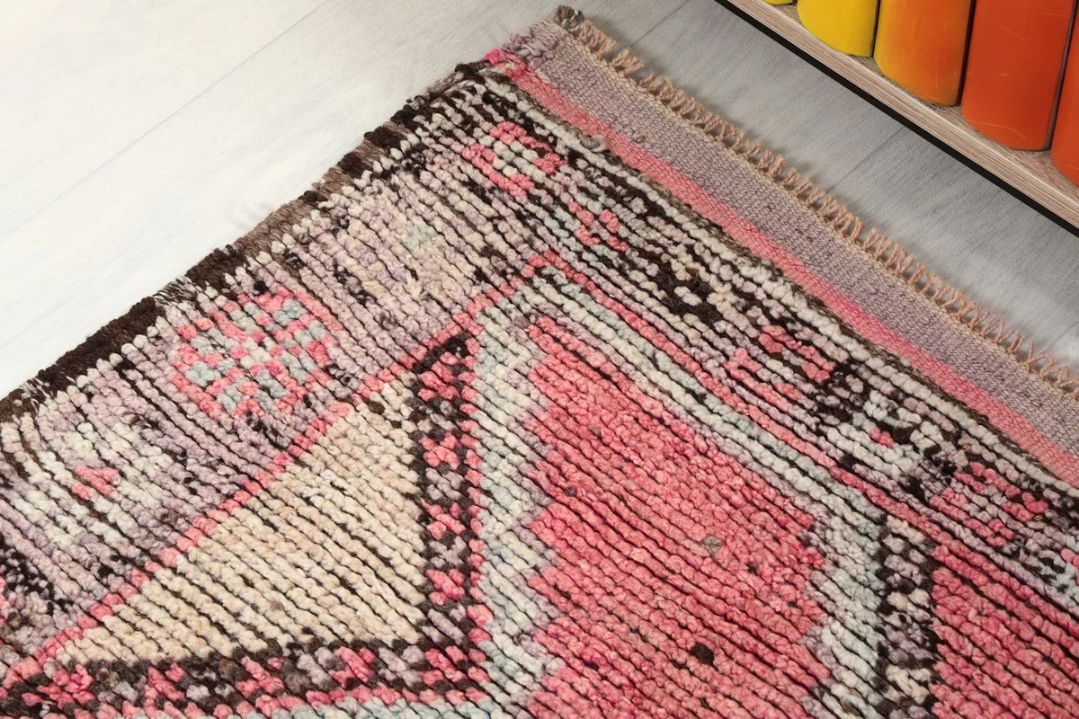 Corner detail of the rug, showing the blend of rose and darker gray tones in the border design