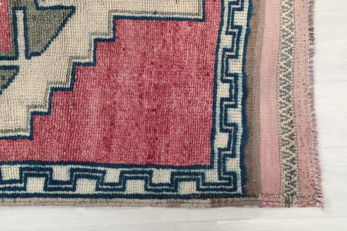 Detail of the rug's border with navy geometric lines and the rose-colored field.