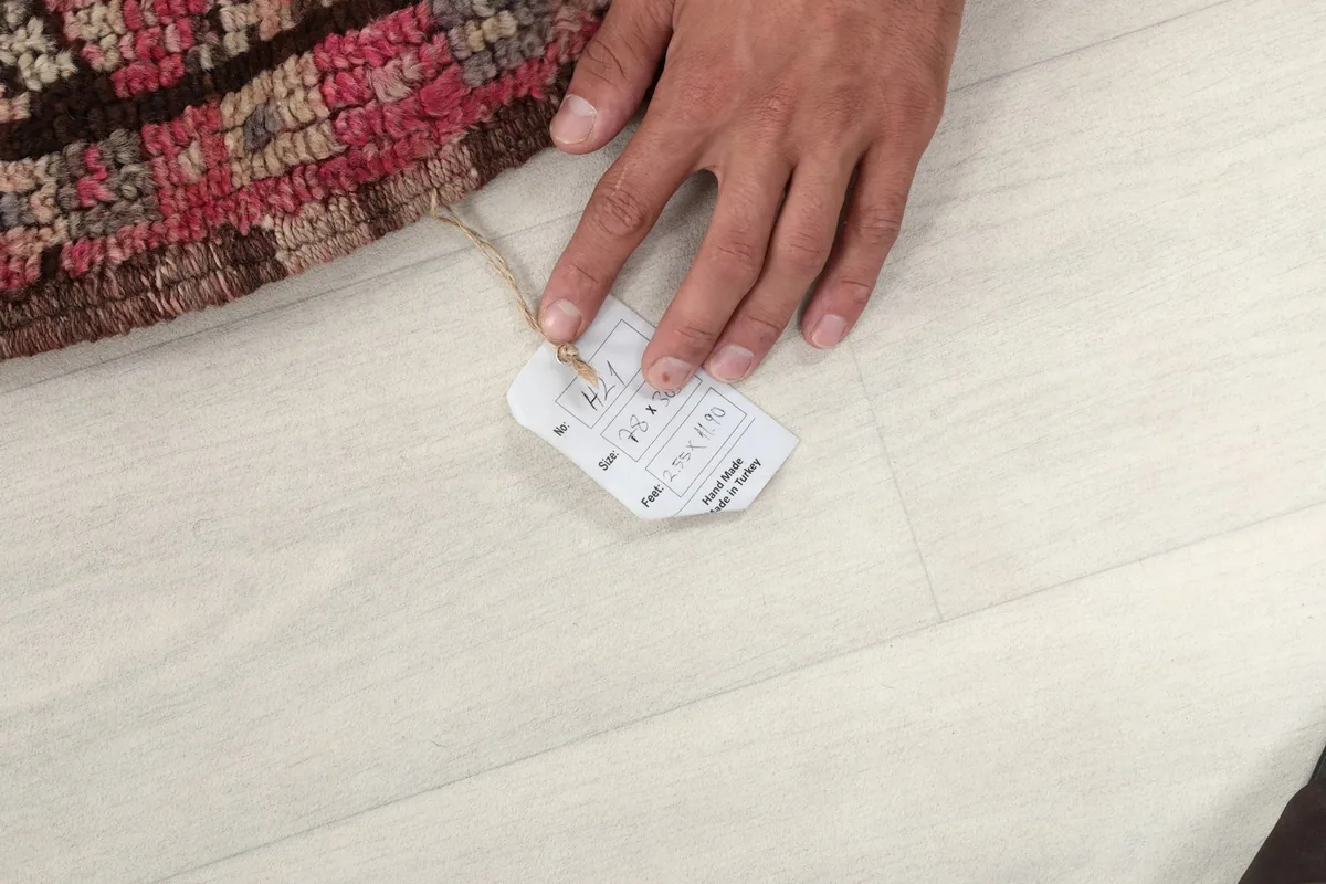 Hand holding the product tag, showing the rug's size and origin details.