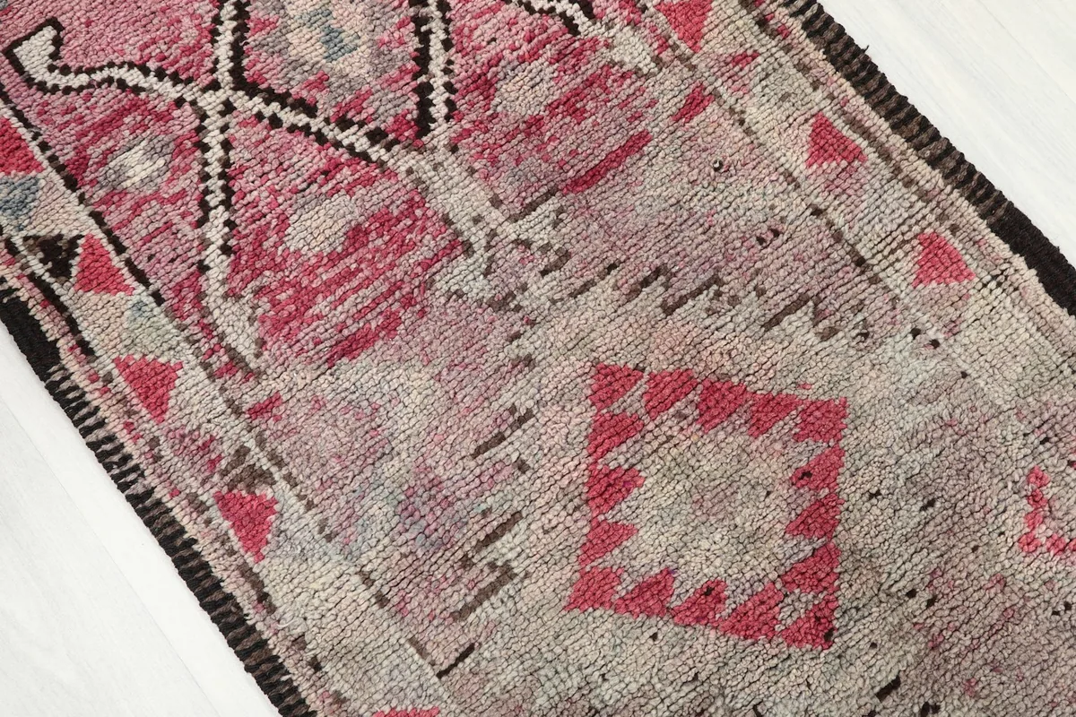 Close-up of the rug's surface showing the faded rose and gray colors and intricate tribal designs