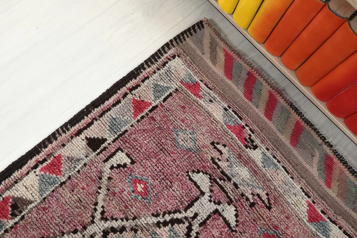 Corner detail of the rug's border, featuring striped patterns in shades of gray, brown, and pink