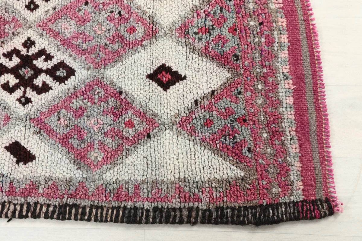 Detailed view of the rug's border and a section of the pink and ivory diamond pattern.