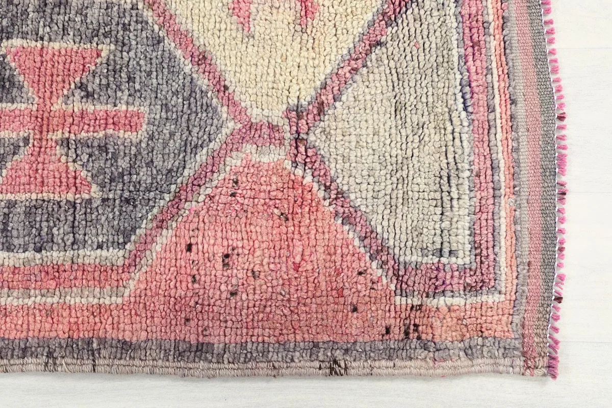 Close-up detail of the hand-knotted wool pile and geometric motif in rose, gray, and pink tones