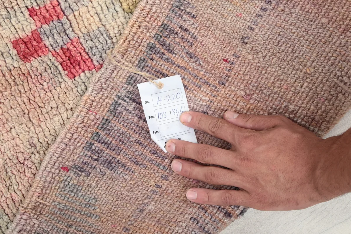 A hand holding a tag with product information, showing the rug's authenticity and material.