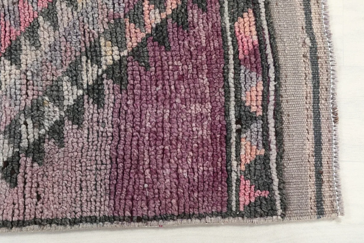 Detail of the rug's short pile, showing variations in rose and purple hues and tribal motifs
