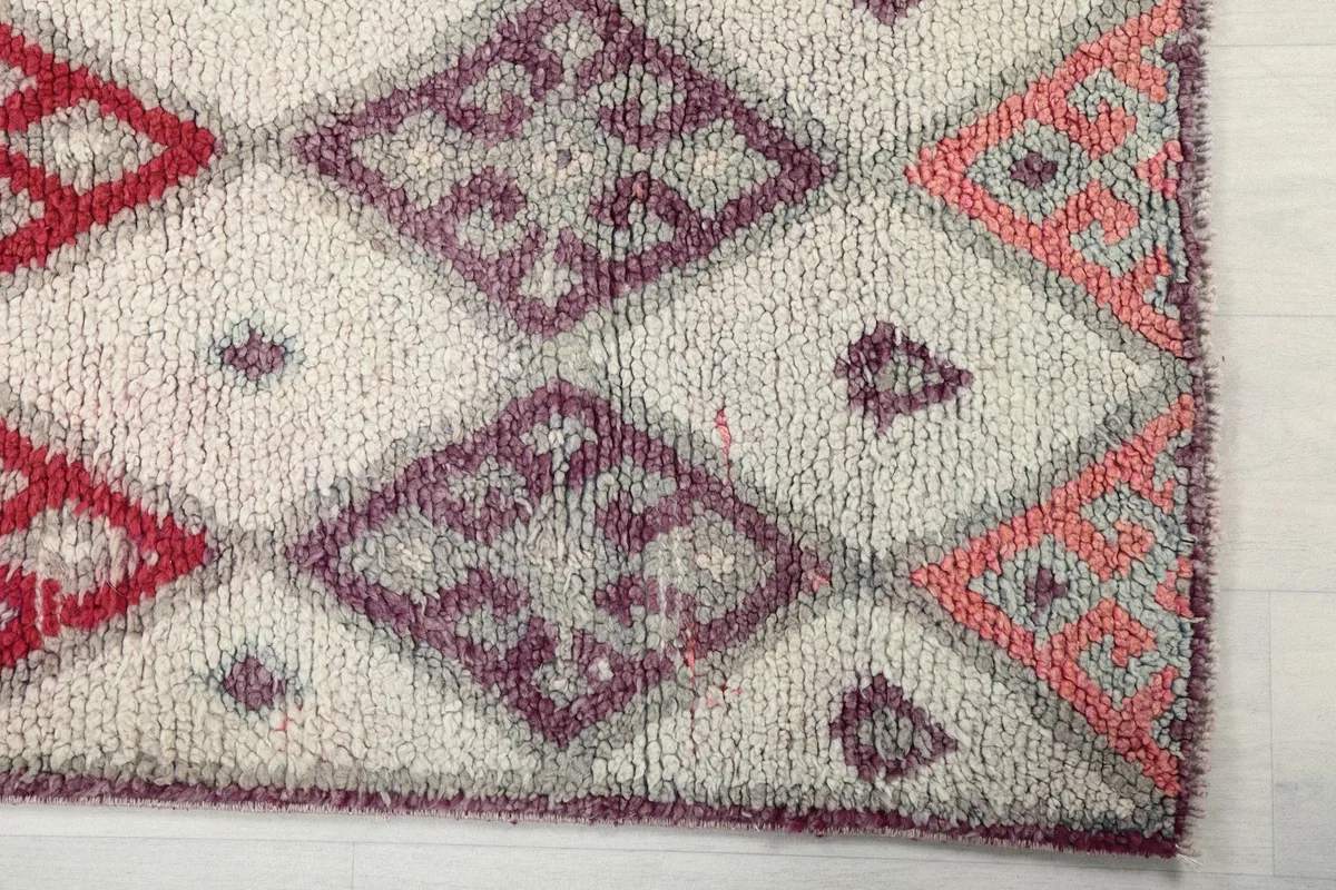 Detailed view of the hand-knotted wool pile and diamond motifs in ivory, purple, and gray
