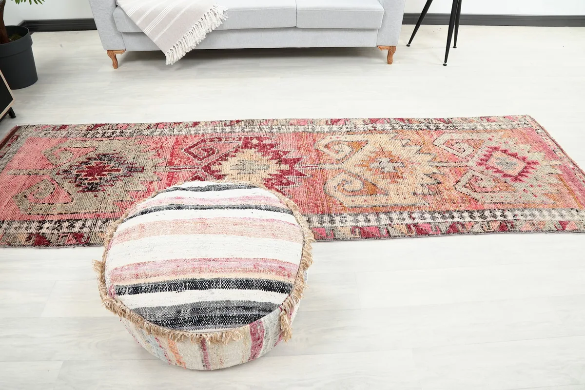 Full length view of the runner rug in a room, positioned with a striped pouf in the foreground.