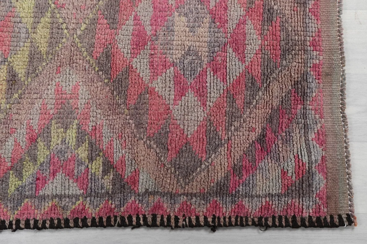 Detailed view of the hand-knotted wool pile and geometric motifs in rose, gray, and yellow tones