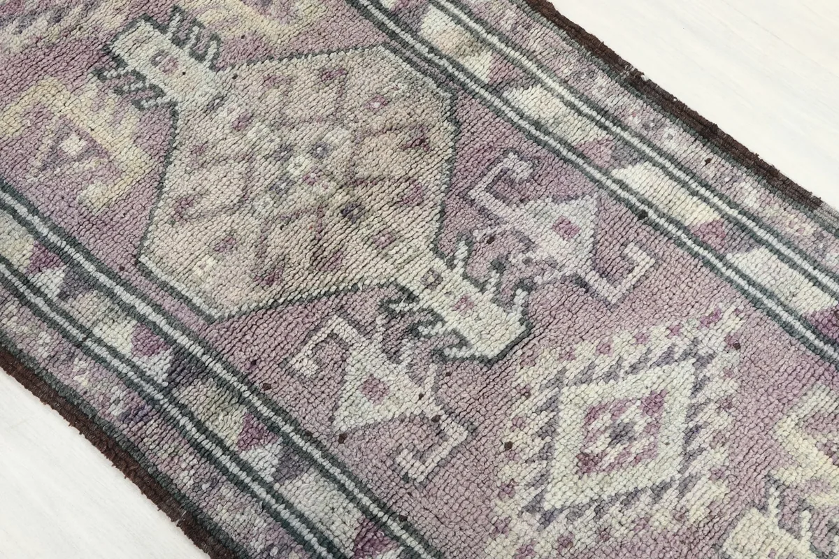 Overhead close-up of the central geometric motifs in rose, ivory, and gray on the runner rug