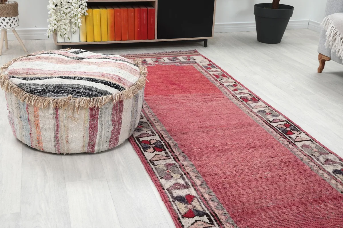 Close-up of the rose runner rug's border next to a striped ottoman in a room