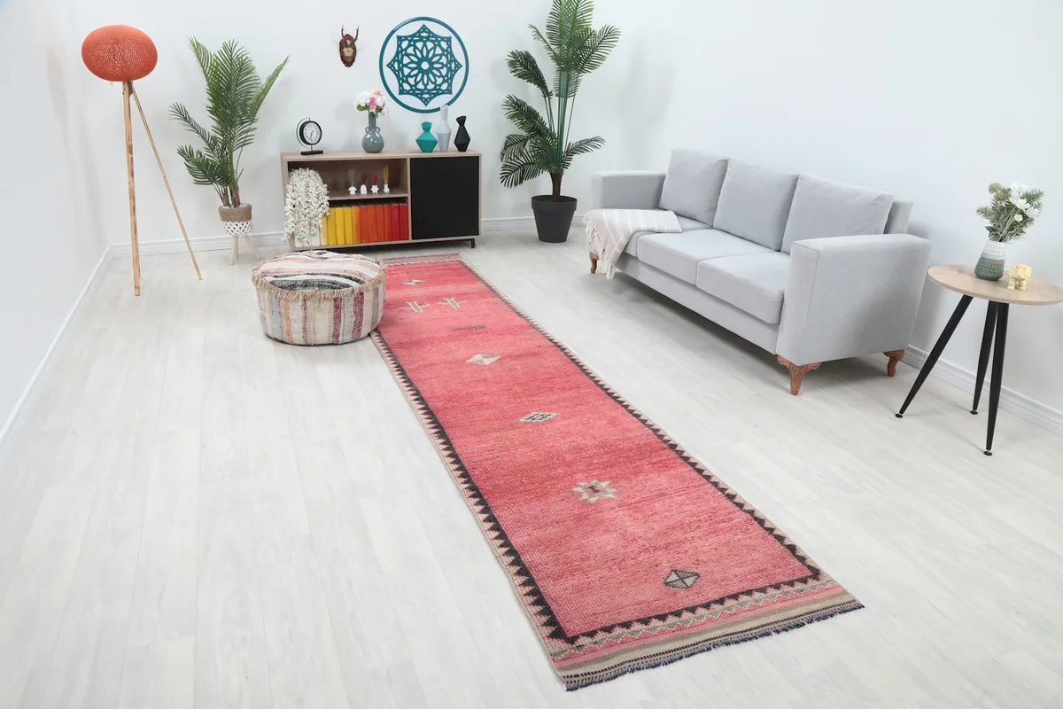 Angle view of the rose runner rug in a room setting, showing its length and placement near a gray sofa.