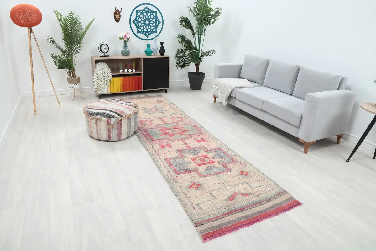 Angle view of the beige and rose runner rug in a room, showing its length next to a gray sofa