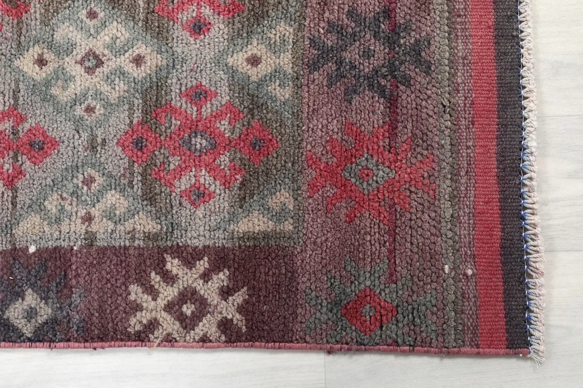 Detailed view of the rug's lower section, showing rose and beige tribal motifs and the border.