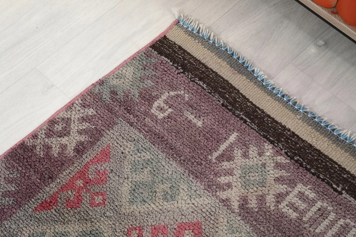 Detail of the rug's upper border and fringe, showing the blend of purple, gray, and beige threads.