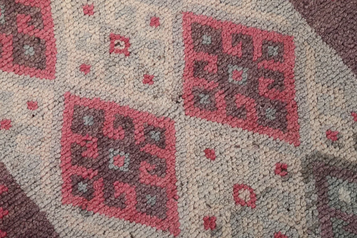 Macro view of the hand-knotted wool pile, revealing the intricate rose and gray tribal design.