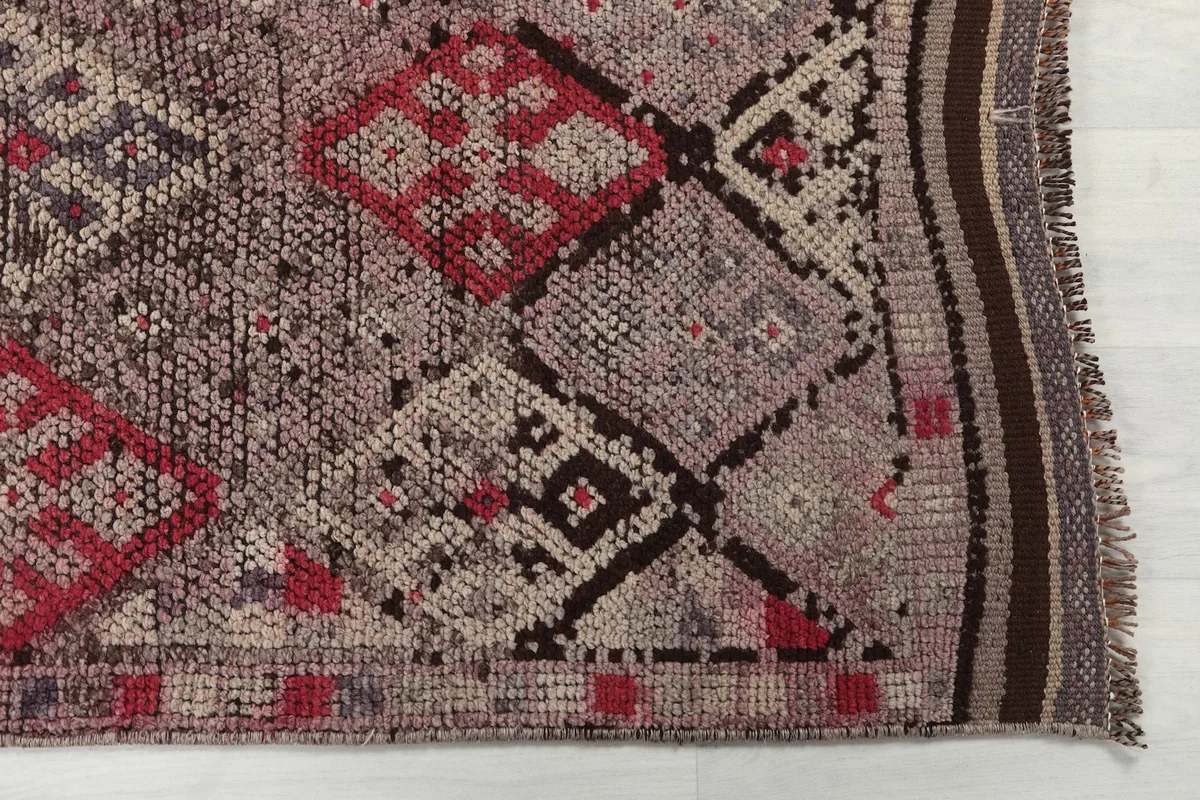 Detailed view of the hand-knotted wool pile, showing rose, red, brown, and ivory tribal motifs