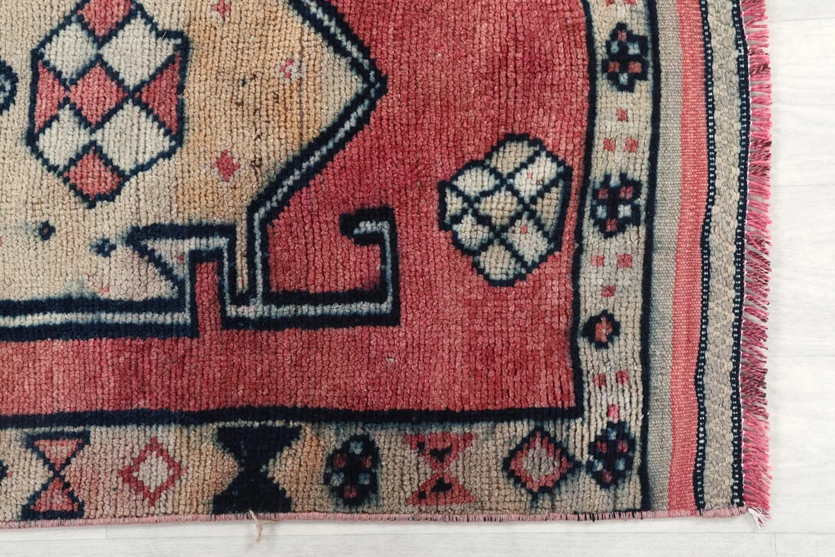 Detail of the rug's border and end, showing the faded rose color and tribal elements