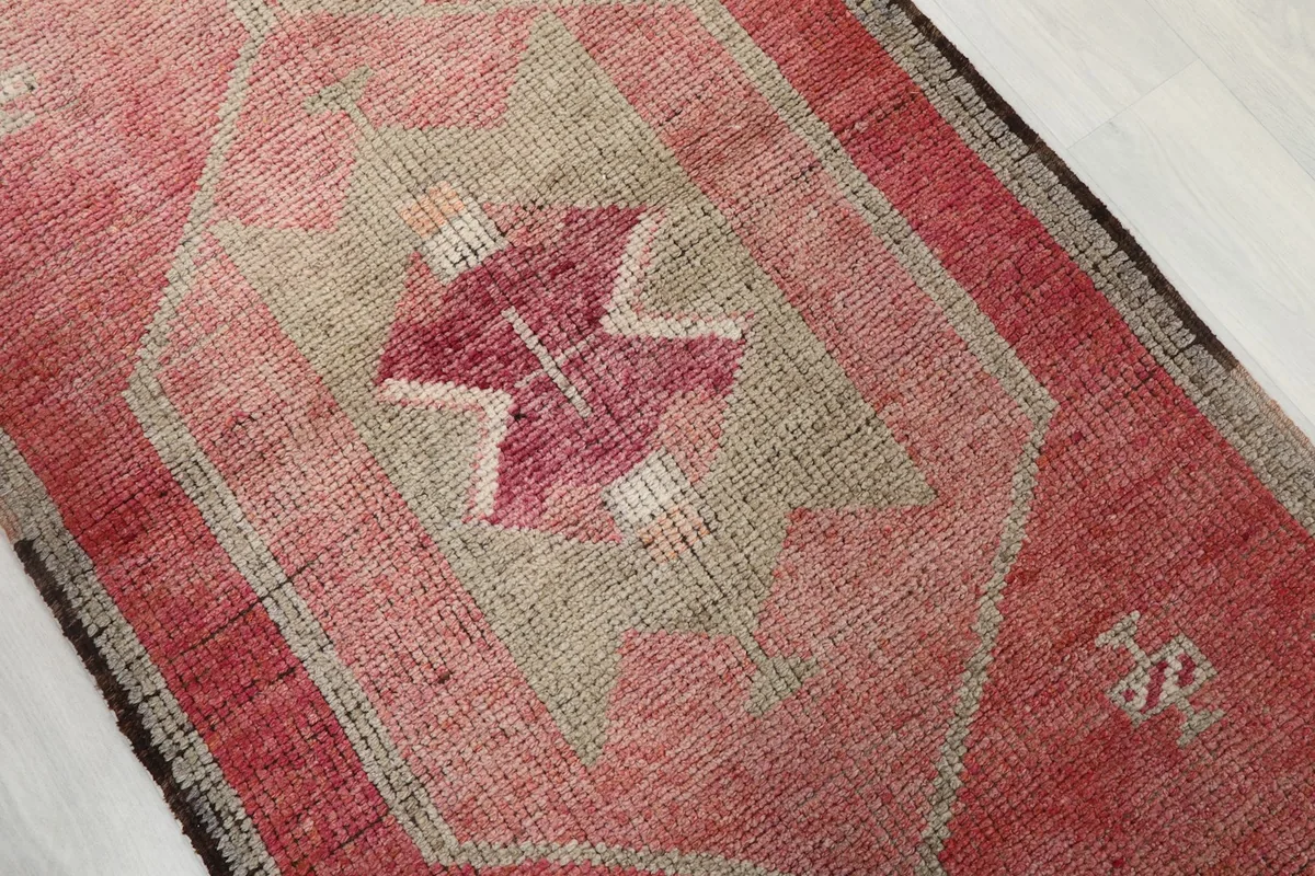 Close-up of a central geometric motif in rose and beige, highlighting the hand-knotted texture