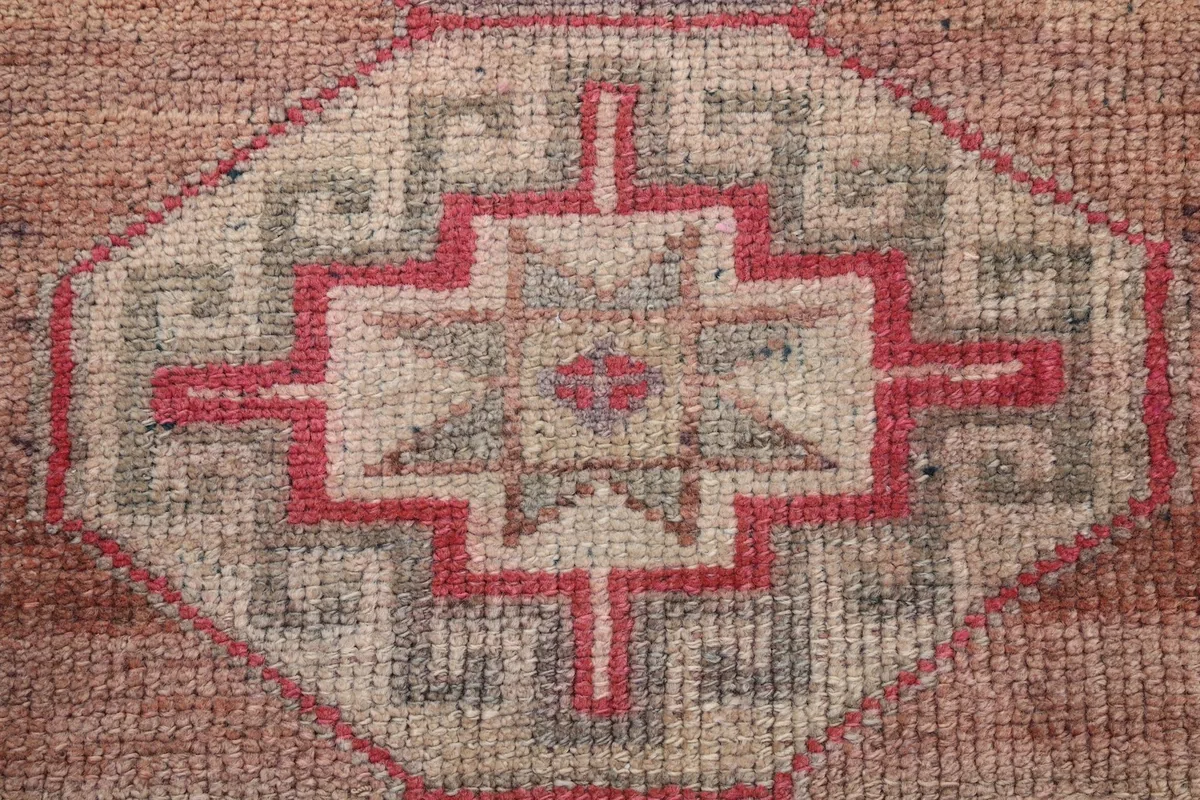Macro detail of a single tribal medallion, showing the intricate knotting and color blend of rose, beige, and gray.