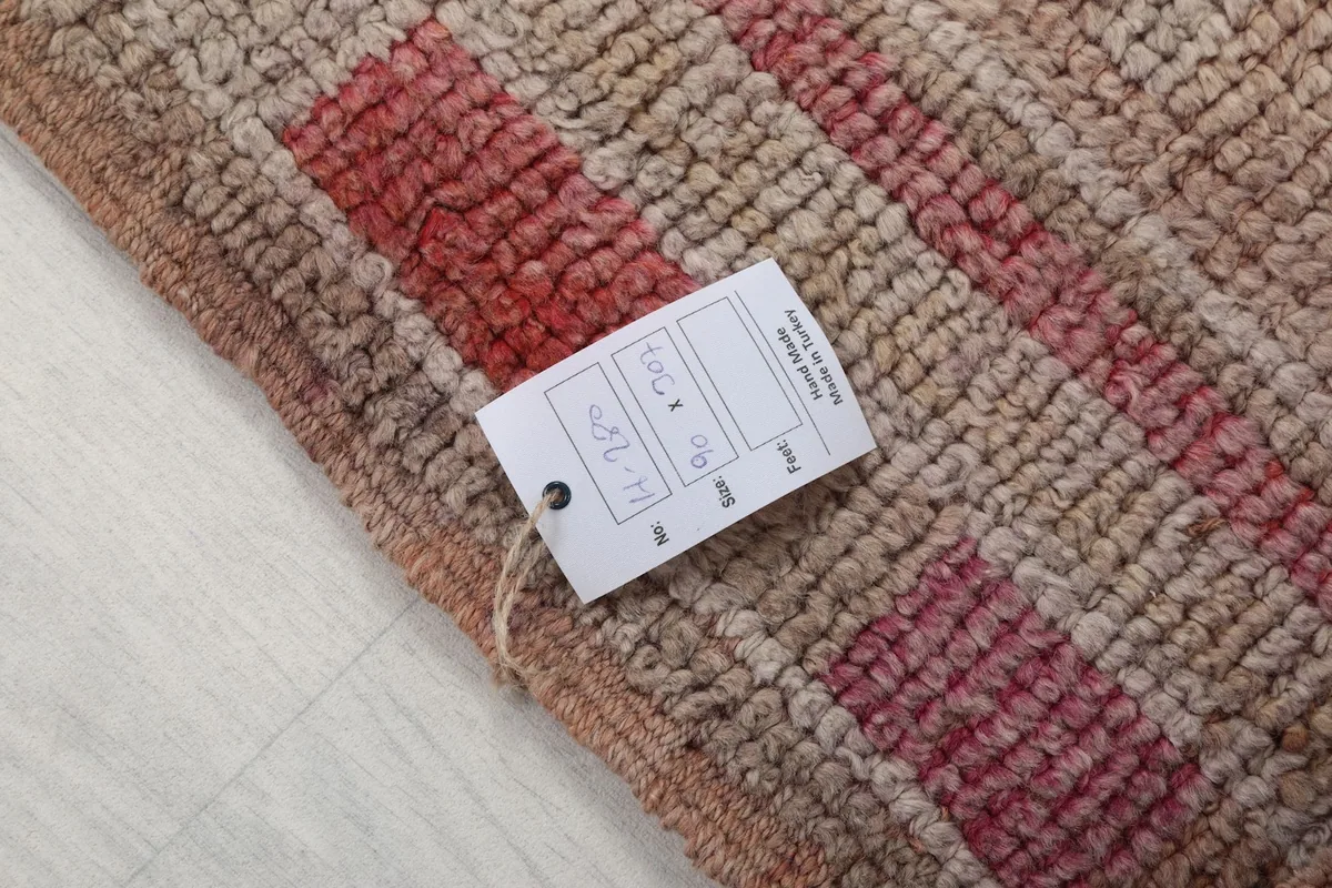 Close-up of the rug's texture with a product tag, showing the low pile and wool fibers