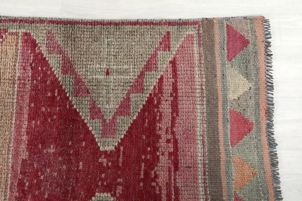 Close-up detail of the rug's end, showing the geometric motifs in rose, gray, and cream with subtle fringe