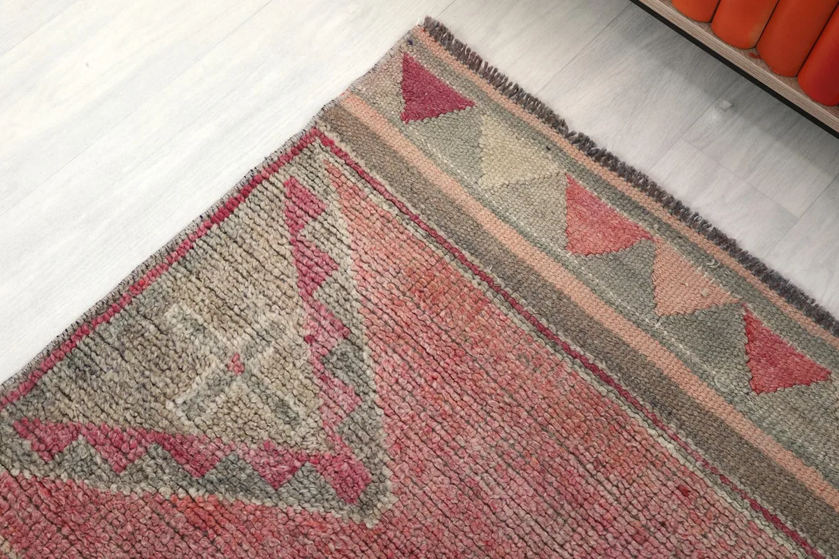 Corner detail of the rug's border, displaying small triangular patterns in various colors and the fringe