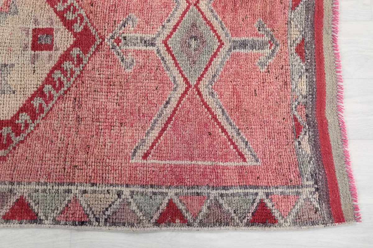 Close-up detail of the rug's end, showing the geometric patterns in rose, gray, and red.