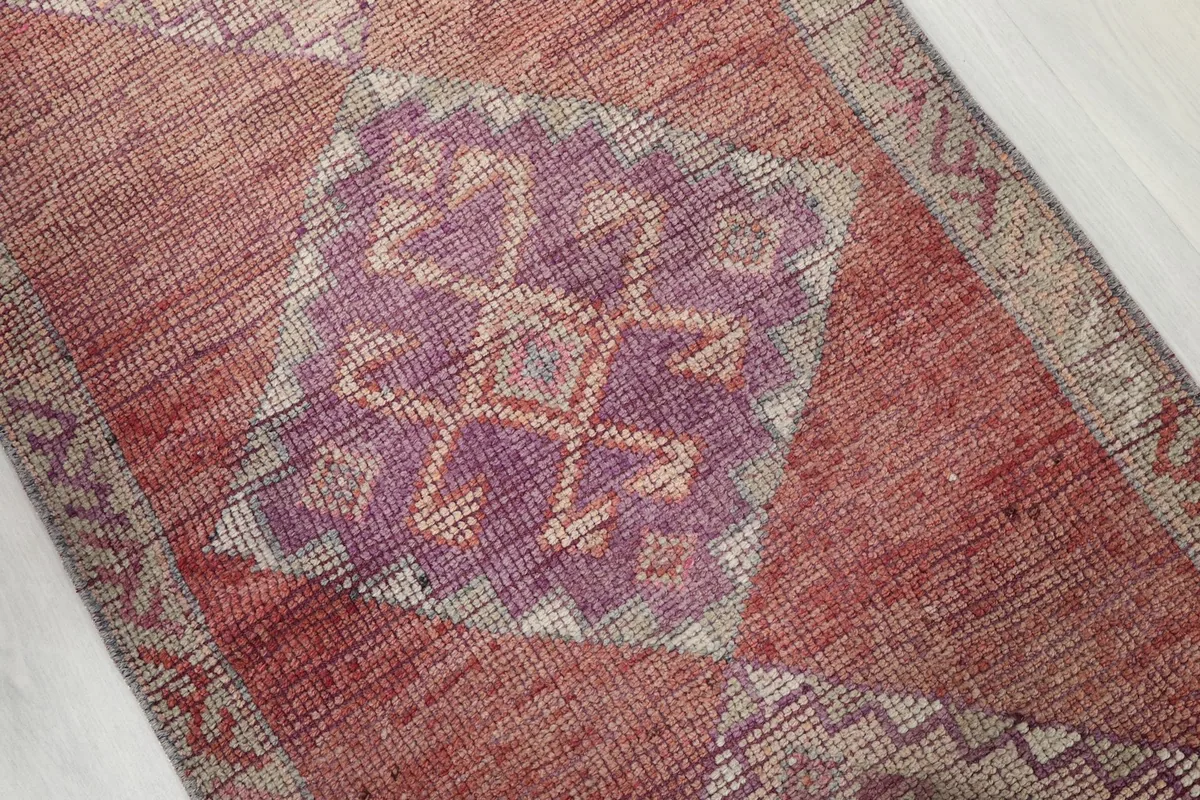 Close-up of a purple geometric diamond motif on the rose field of the vintage Anatolian runner