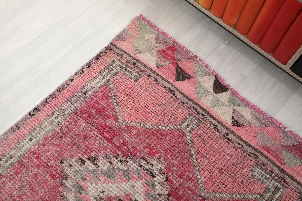 Corner detail of the runner rug's border with triangular motifs in rose, gray, and red