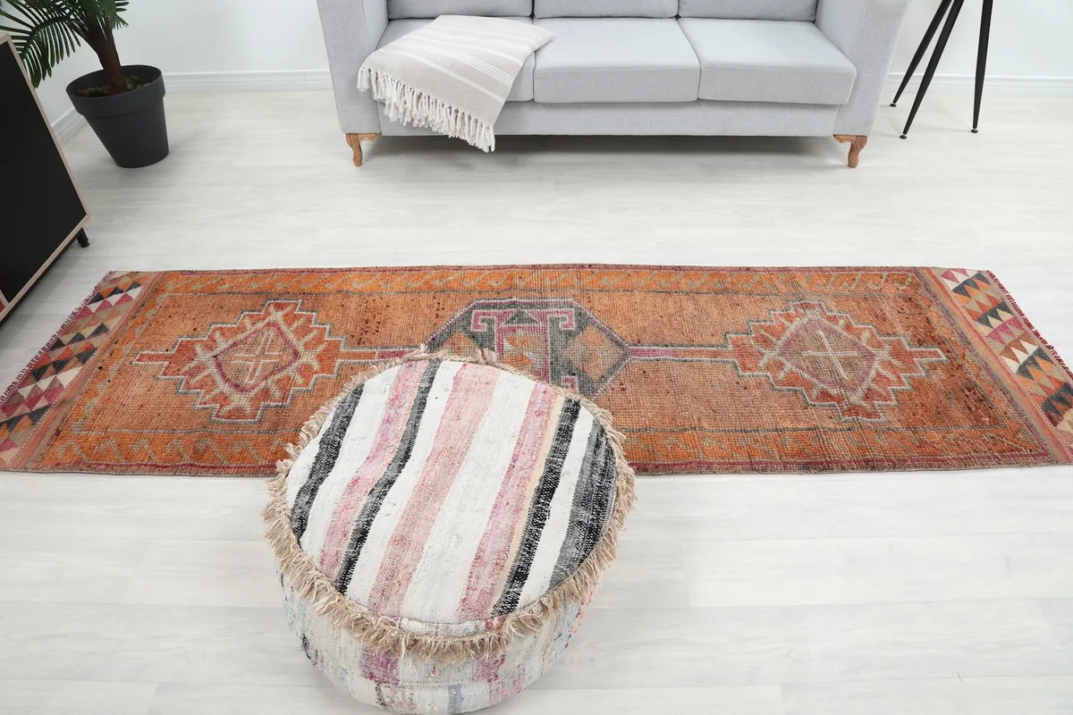 Full overhead view of the orange runner rug in a room, with a pouf in the foreground