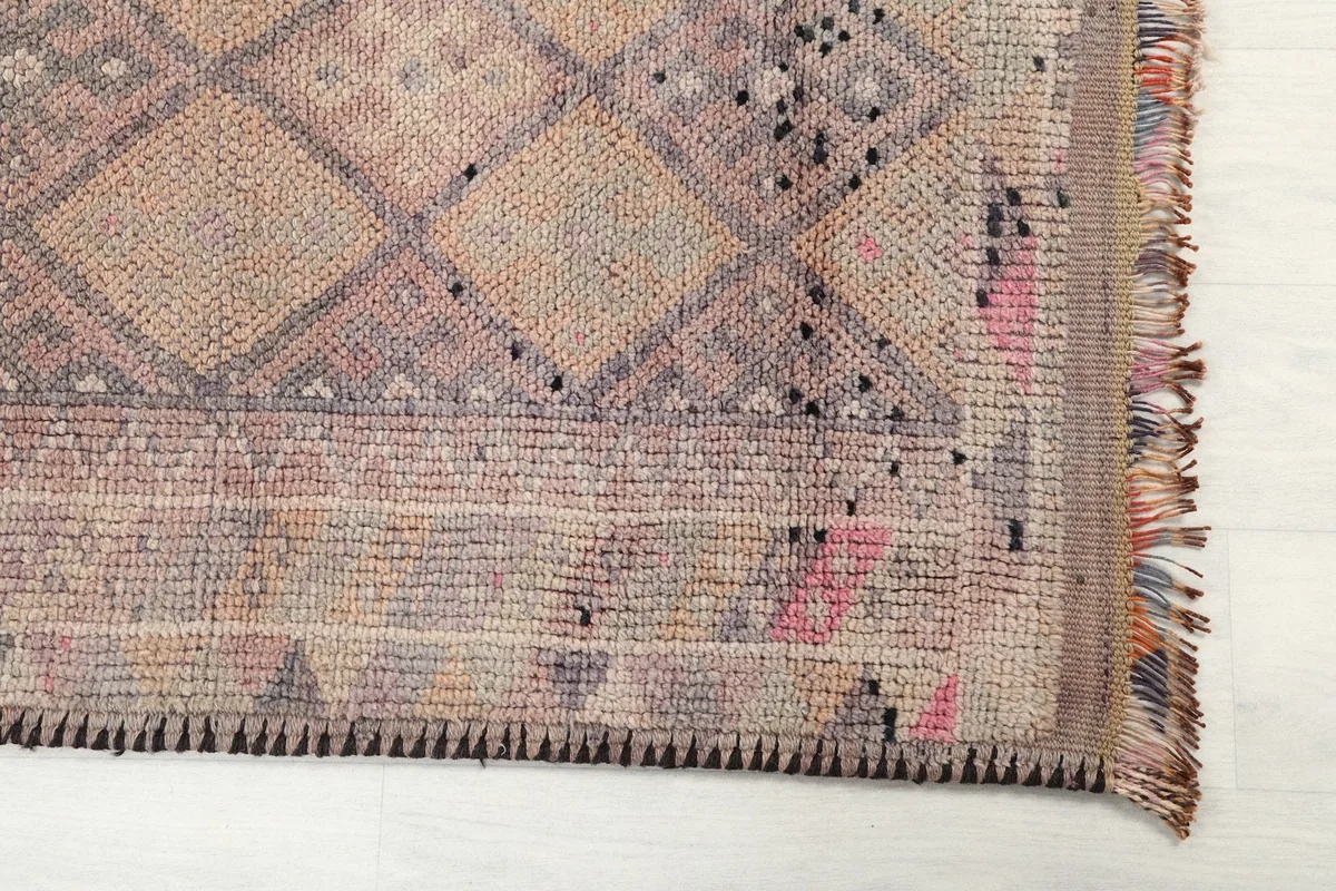 Close-up of the rug's end, showing the fringe and edge stitching with a hint of rose and gray tones