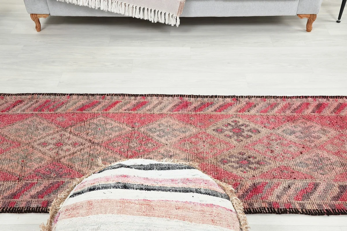 Faded red geometric runner rug in a room setting, with a sofa and ottoman nearby.