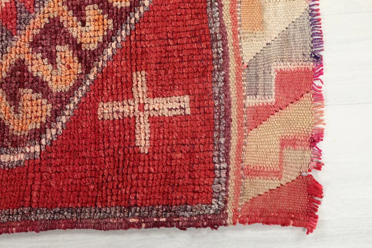 Detailed view of the red field and a light beige cross motif, showing the rug's edge.